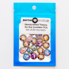 Package of handcrafted tokens for the Gundam Trading Card Game. The blue packaging features a clear window displaying 20 colorful circular counters labeled with gameplay symbols. The label reads: "Battle Baubles – Handcrafted Tokens for the Gundam TCG – Set of 20 Counters."