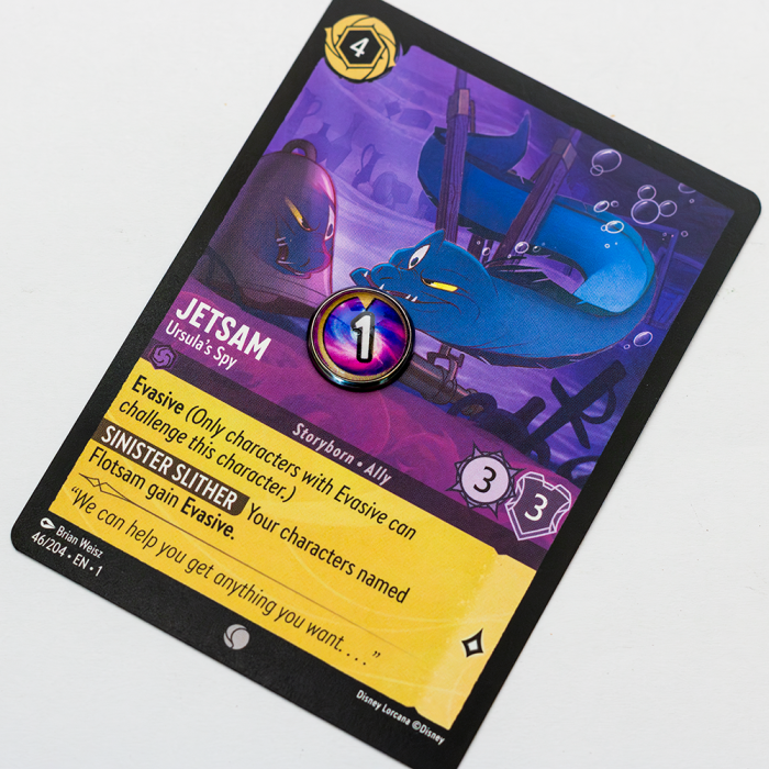 Lorcana Damage 3 Lorcana trading card featuring Jetsam, labeled as 'Storyborn – Ally' and 'Ursula’s Spy'. The card shows a blue eel-like creature swimming near a shipwreck. Gameplay details include Cost 4 ink, Strength 3, Willpower 3, and 1 Damage (marked by a circular token). Abilities include 'Evasive' and 'Sinister Slither', which grants Evasive to characters named Flotsam.